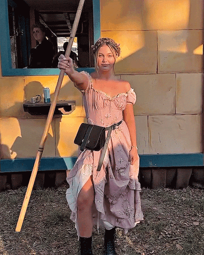 A Woman In A Pink Dress Holds A Wooden Stick GIF