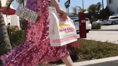 A Woman In A Pink Dress Is Carrying A Bag That Says In-N-Out GIF