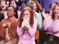 A Woman In A Pink Dress Is Covering Her Mouth While Sitting In A Crowd Of People . GIF