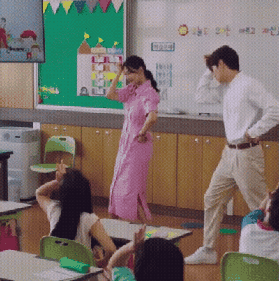 A Woman In A Pink Dress Is Dancing In A Classroom With A Sign That Says " Sun " On It GIF