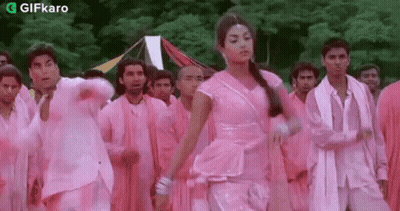 A Woman In A Pink Dress Is Dancing In Front Of A Group Of Men In Pink Clothes . GIF