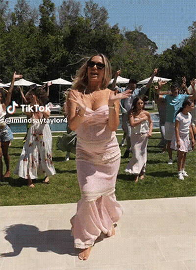 A Woman In A Pink Dress Is Dancing In Front Of A Group Of People With A Tik Tok Watermark GIF