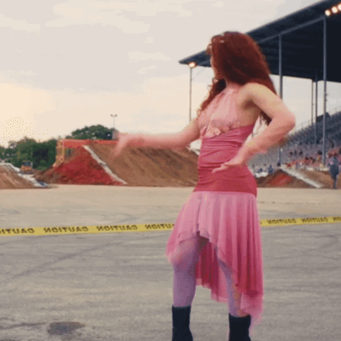 A Woman In A Pink Dress Is Dancing In Front Of A Yellow Caution Tape That Says " Hoituad " GIF