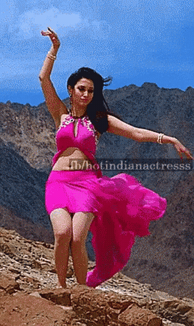 A Woman In A Pink Dress Is Dancing On A Rocky Hillside With Mountains In The Background And The Caption Hotindianactress GIF