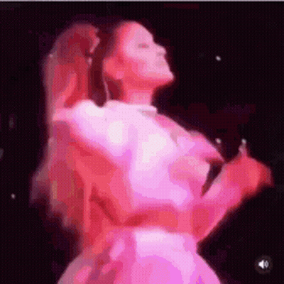 A Woman In A Pink Dress Is Dancing On A Stage While Holding A Microphone . GIF