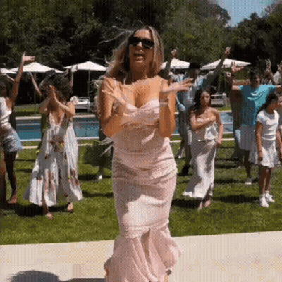 A Woman In A Pink Dress Is Dancing With A Group Of People In A Backyard . GIF