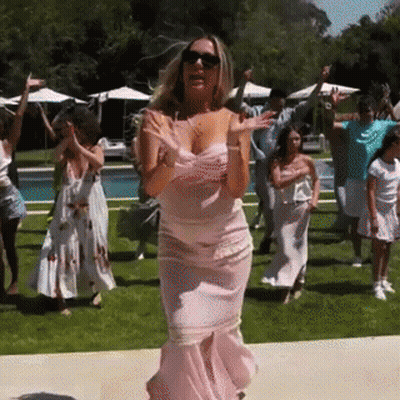 A Woman In A Pink Dress Is Dancing With A Group Of People In Front Of A Swimming Pool . GIF