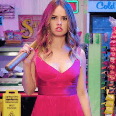 A Woman In A Pink Dress Is Holding A Bat Over Her Shoulder In Front Of A Sign That Says Caution Wet Floor GIF