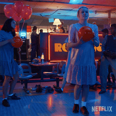 A Woman In A Pink Dress Is Holding A Bowling Ball In A Bowling Alley With Netflix Written On The Bottom GIF