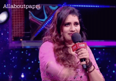 A Woman In A Pink Dress Is Holding A Microphone In Front Of A Sign That Says Allaboutpapri GIF