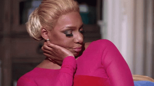 A Woman In A Pink Dress Is Holding Her Hand To Her Face . GIF