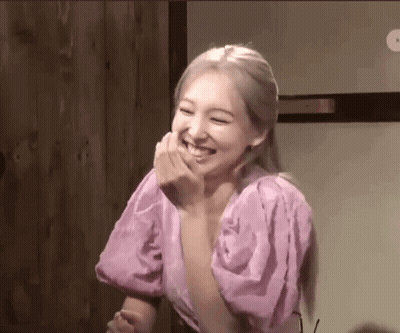 A Woman In A Pink Dress Is Laughing With Her Hand Over Her Mouth . GIF