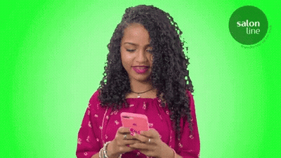 A Woman In A Pink Dress Is Looking At Her Cell Phone GIF