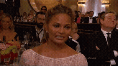 A Woman In A Pink Dress Is Making A Funny Face While Sitting In A Crowd Of People . GIF