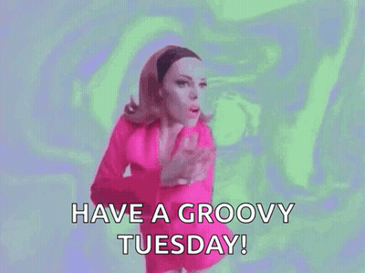 A Woman In A Pink Dress Is Saying `` Have A Groovy Tuesday '' . GIF