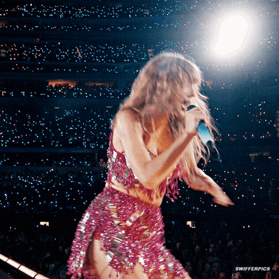 A Woman In A Pink Dress Is Singing Into A Microphone On A Stage GIF