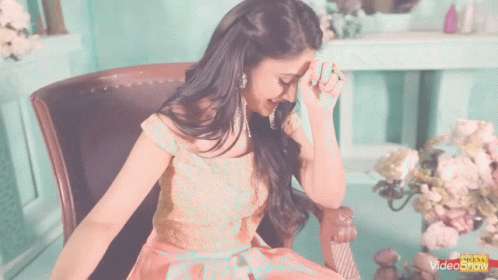 A Woman In A Pink Dress Is Sitting In A Chair And Covering Her Face With Her Hands GIF