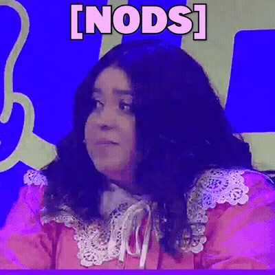 A Woman In A Pink Dress Is Sitting In Front Of A Blue Wall With The Word Nods Written On It . GIF