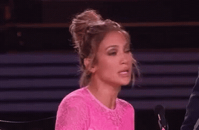 A Woman In A Pink Dress Is Sitting In Front Of A Microphone And Making A Face . GIF