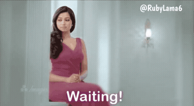 A Woman In A Pink Dress Is Sitting In Front Of A Wall That Says Waiting GIF
