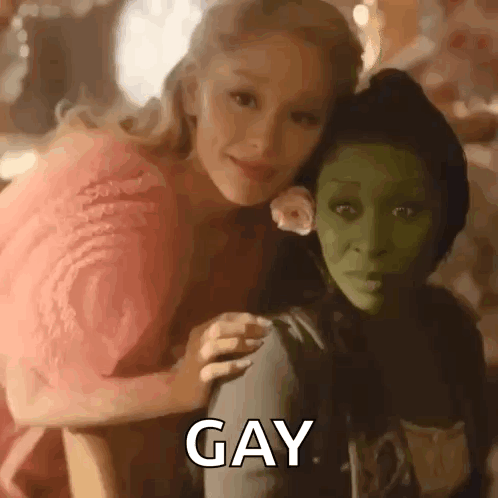 A Woman In A Pink Dress Is Sitting Next To A Green Woman In A Green Mask . GIF