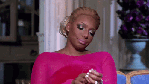 A Woman In A Pink Dress Is Sitting On A Couch Holding A Necklace And A Ring . GIF