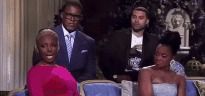 A Woman In A Pink Dress Is Sitting On A Couch Next To Two Men In Suits . GIF