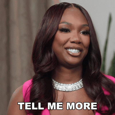 A Woman In A Pink Dress Is Smiling And Says " Tell Me More " GIF