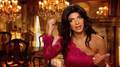 A Woman In A Pink Dress Is Standing In A Dining Room With A Fist In The Air . GIF