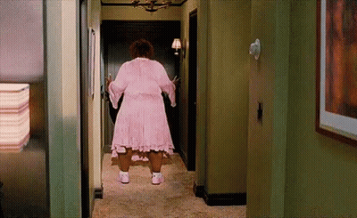 A Woman In A Pink Dress Is Standing In A Hallway . GIF