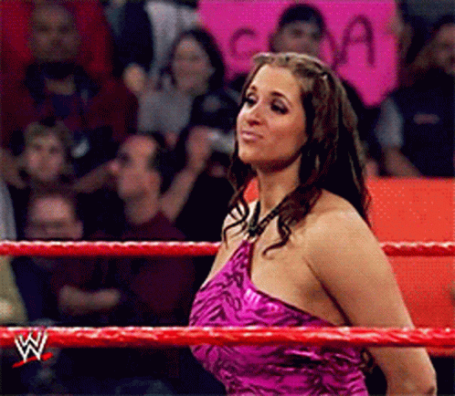 A Woman In A Pink Dress Is Standing In A Wrestling Ring With A W Logo On The Ropes GIF