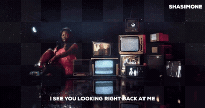 A Woman In A Pink Dress Is Standing In Front Of A Bunch Of Televisions With The Words I See You Looking Right Back GIF