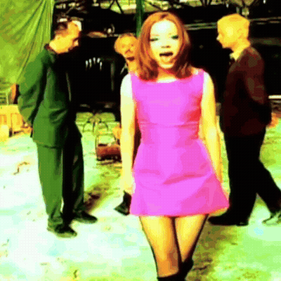 A Woman In A Pink Dress Is Standing In Front Of A Group Of People GIF