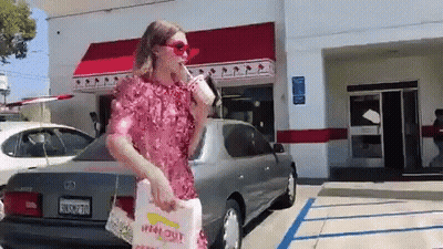 A Woman In A Pink Dress Is Standing In Front Of A In-N-Out Restaurant GIF