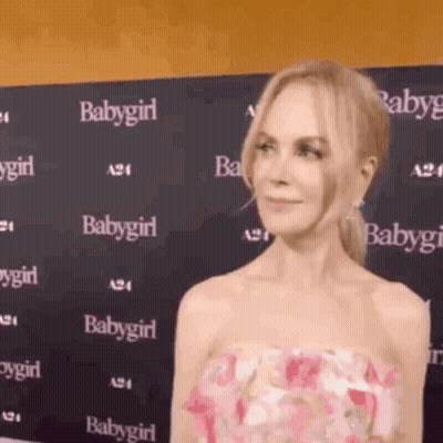 A Woman In A Pink Dress Is Standing In Front Of A Wall That Says Babygirl On It . GIF
