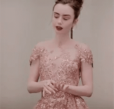 A Woman In A Pink Dress Is Standing In Front Of A White Wall . GIF