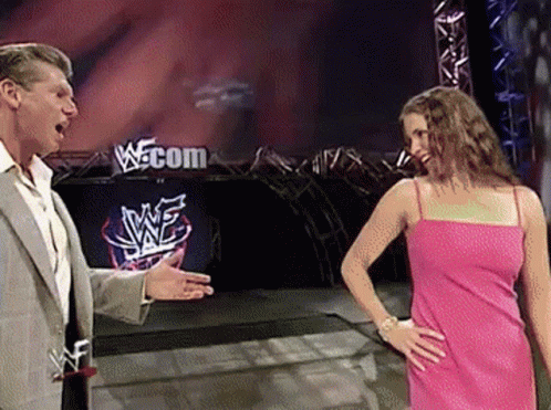 A Woman In A Pink Dress Is Standing Next To A Man In A Suit In Front Of A Sign That Says Wwe.com GIF