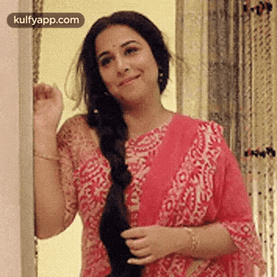 A Woman In A Pink Dress Is Standing Next To A Wall And Smiling . GIF