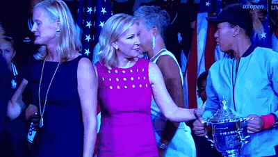 A Woman In A Pink Dress Is Standing Next To A Woman Holding A Trophy GIF