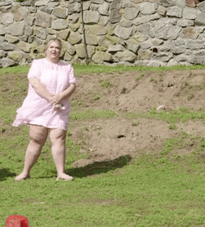 A Woman In A Pink Dress Is Standing On A Grassy Hill . GIF