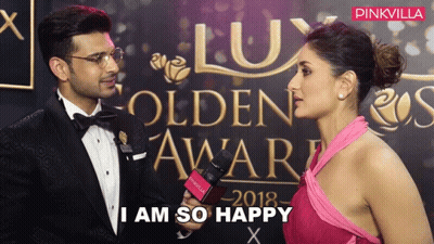 A Woman In A Pink Dress Is Talking To A Man In A Tuxedo In Front Of A Wall That Says Lux GIF