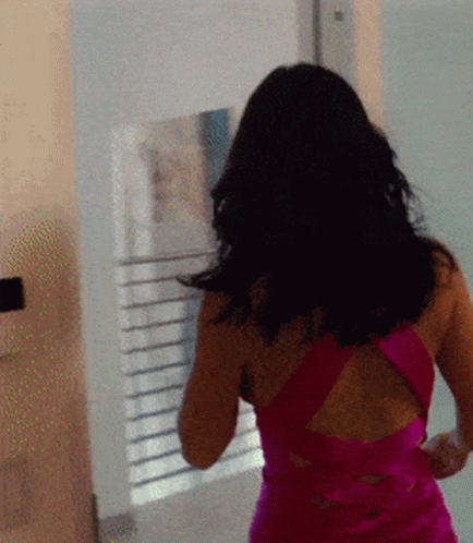 A Woman In A Pink Dress Is Walking In Front Of A Window GIF