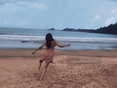 A Woman In A Pink Dress Is Walking On A Beach With The Name Mambazalien On The Sand GIF