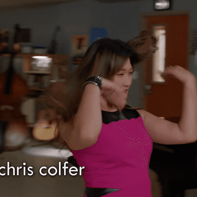 A Woman In A Pink Dress Stands In Front Of A Piano With The Name Chris Colfer On The Bottom GIF