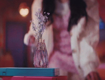 A Woman In A Pink Dress Stands In Front Of A Vase Of Flowers GIF