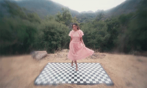 A Woman In A Pink Dress Stands On A Checkered Rug GIF