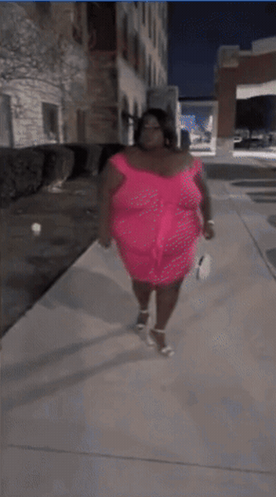 A Woman In A Pink Dress Stands On A Sidewalk GIF