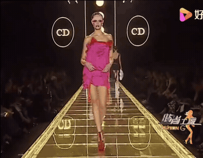 A Woman In A Pink Dress Walks Down A Runway With The Letters Cd On The Side GIF