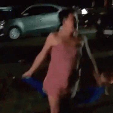 A Woman In A Pink Dress With A Bow On The Back Is Walking Down A Street At Night . GIF