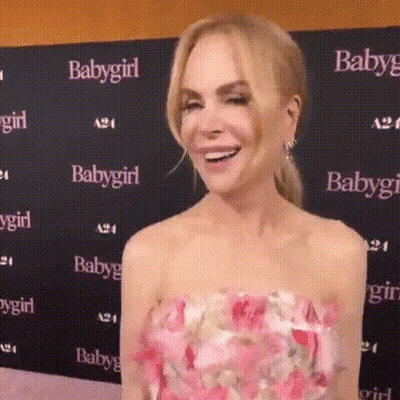 A Woman In A Pink Floral Dress Is Smiling In Front Of A Baby Girl Sign . GIF